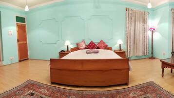 Quarto com uma cama grande, guarda-roupa de madeira, sofá estampado e abajur.