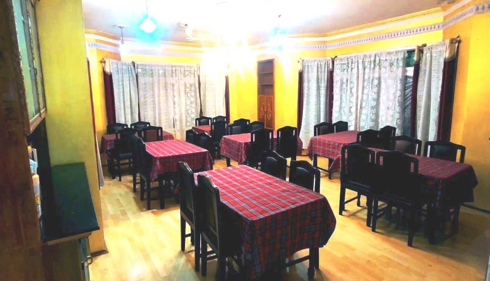 Uma sala de jantar com mesas e cadeiras, paredes amarelas e cortinas estampadas.