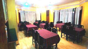 Uma sala de jantar com mesas e cadeiras, paredes amarelas e cortinas estampadas.