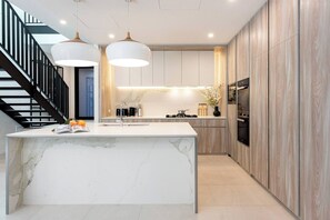 A modern kitchen with a marble island, pendant lights, and a built-in oven. - Sunny Townhouse Style Apartment at Bondi (Bondi)