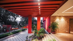 A covered outdoor area with a tiled floor, red structural columns, and potted plants.