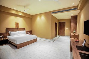A hotel room with a large bed, a desk with a flat-screen TV, a ceiling fan, and a small Christmas tree. - Gulab Kothi By Grapevine Varanasi (Kashipur)