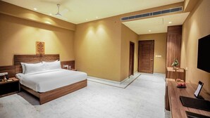 A hotel room with a large bed, a desk with a flat-screen TV, a ceiling fan, and a small Christmas tree.