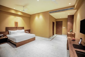 A hotel room with a large bed, a desk with a flat-screen TV, a ceiling fan, and a small Christmas tree.