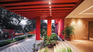 Un espacio al aire libre cubierto con suelo de baldosas, columnas estructurales rojas y plantas en macetas.