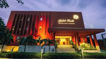A modern building with a prominent entrance, a sign reading 'Gulab Kothi Boutique Hotel & Banquets,' and a well-lit facade.