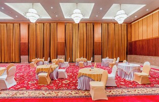 Un salón de conferencias con mesas redondas, sillas blancas y alfombra roja.