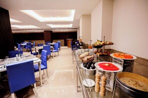A hotel dining area with multiple tables, chairs, and a buffet with various food items.
