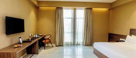 A hotel room with a bed, desk, chair, television, and large windows with curtains.