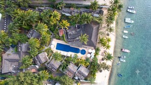 Vista aérea de un resort con piscina, varias edificaciones y una playa con barcos.