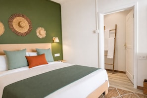 Habitación de hotel con cama, almohadas, una lámpara de pared y una puerta que da a un baño.