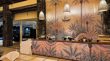 A reception area with a decorative wall featuring palm trees and a fisherman, a counter with a woven lamp, and a tiled floor.