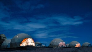 A series of dome-shaped structures with a central illuminated space, set against a night sky. - Sun City Camp (Wadi Rum)