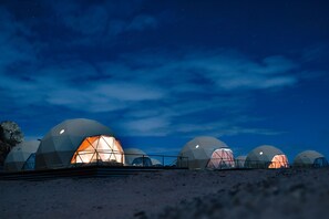A series of dome-shaped structures with a central illuminated space, set against a night sky. - Sun City Camp (Wadi Rum)