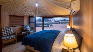 A room with a bed, a chair, a lamp, and a view of yurts outside. - Sun City Camp (Wadi Rum)