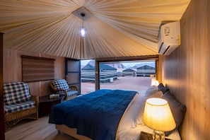 A room with a bed, a chair, a lamp, and a view of yurts outside. - Sun City Camp (Wadi Rum)
