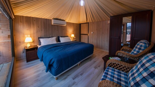 A bedroom with a bed, bedside lamps, a chair, and a wardrobe. - Sun City Camp (Wadi Rum)