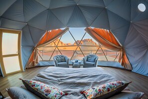 A tented accommodation with a bed, two chairs, and a view of a desert landscape. - Sun City Camp (Wadi Rum)