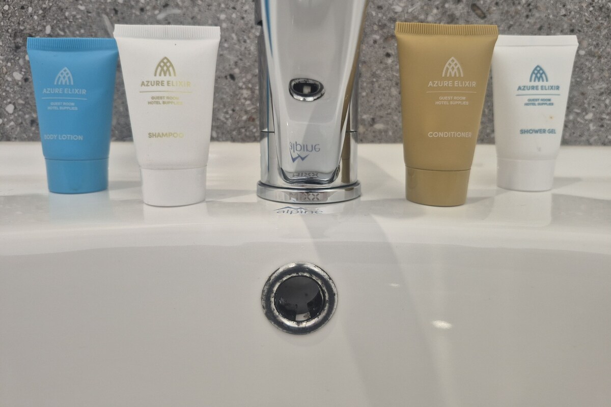 A sink with toiletries including body lotion, shampoo, conditioner, and shower gel.