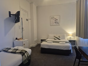 A hotel room with a bed, a desk, a chair, a TV mounted on the wall, and a door. - The Freemasons Hotel (Bridgetown)