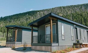 A two-story cabin with a covered porch and a mountain backdrop. - Terra Nova Cabins (West Yellowstone)