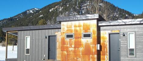 Reihenweise Holzhütten mit Metallverkleidung, einer Holzdielen-Terrasse und einem Berg im Hintergrund.