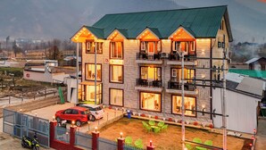 A multi-story hotel with balconies, a parking area, and a view of mountains. - Classy Castle (Anantnag)