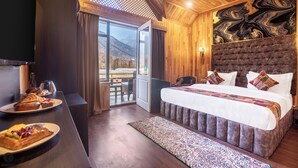 A hotel room with a large bed, a dining area with pastries, and a view of mountains through the window. - Classy Castle (Anantnag)