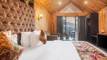 A bedroom with a large bed, a wooden headboard, a view through an open door, and a small table with a bottle and glasses.