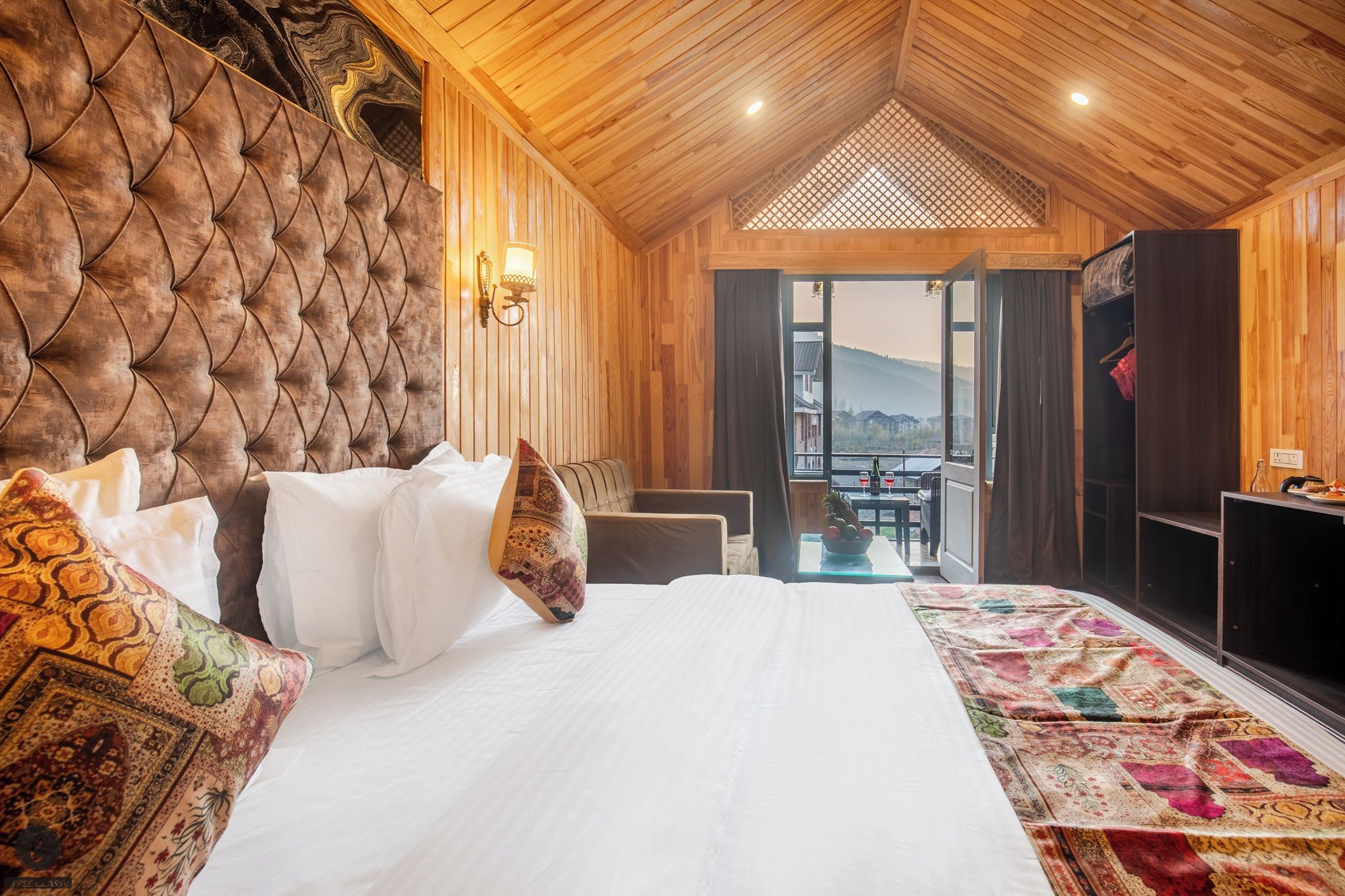 Un dormitorio con una cama grande, cabecera de madera, vista a través de una puerta abierta y una pequeña mesa con una botella y vasos.