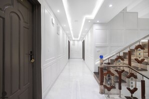 A hallway with a staircase, white walls, and a door on the left. - Classy Castle (Anantnag)