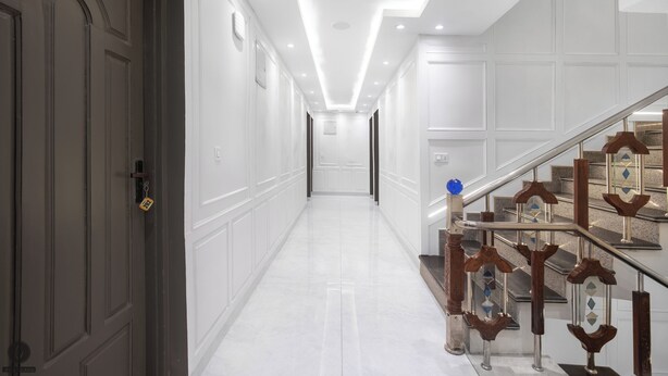 A hallway with a staircase, white walls, and a door on the left. - Classy Castle (Anantnag)
