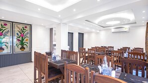 A hotel dining area with multiple tables and chairs, a decorative wall with floral artwork, and recessed ceiling lighting. - Classy Castle (Anantnag)