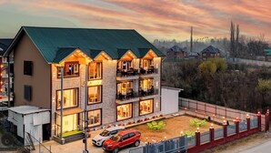 A multi-story hotel with balconies, a parking area, and a view of the surrounding landscape. - Classy Castle (Anantnag)