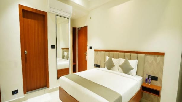 Una habitación de hotel con una cama grande, cabecera de madera, mesita de noche y un espejo.