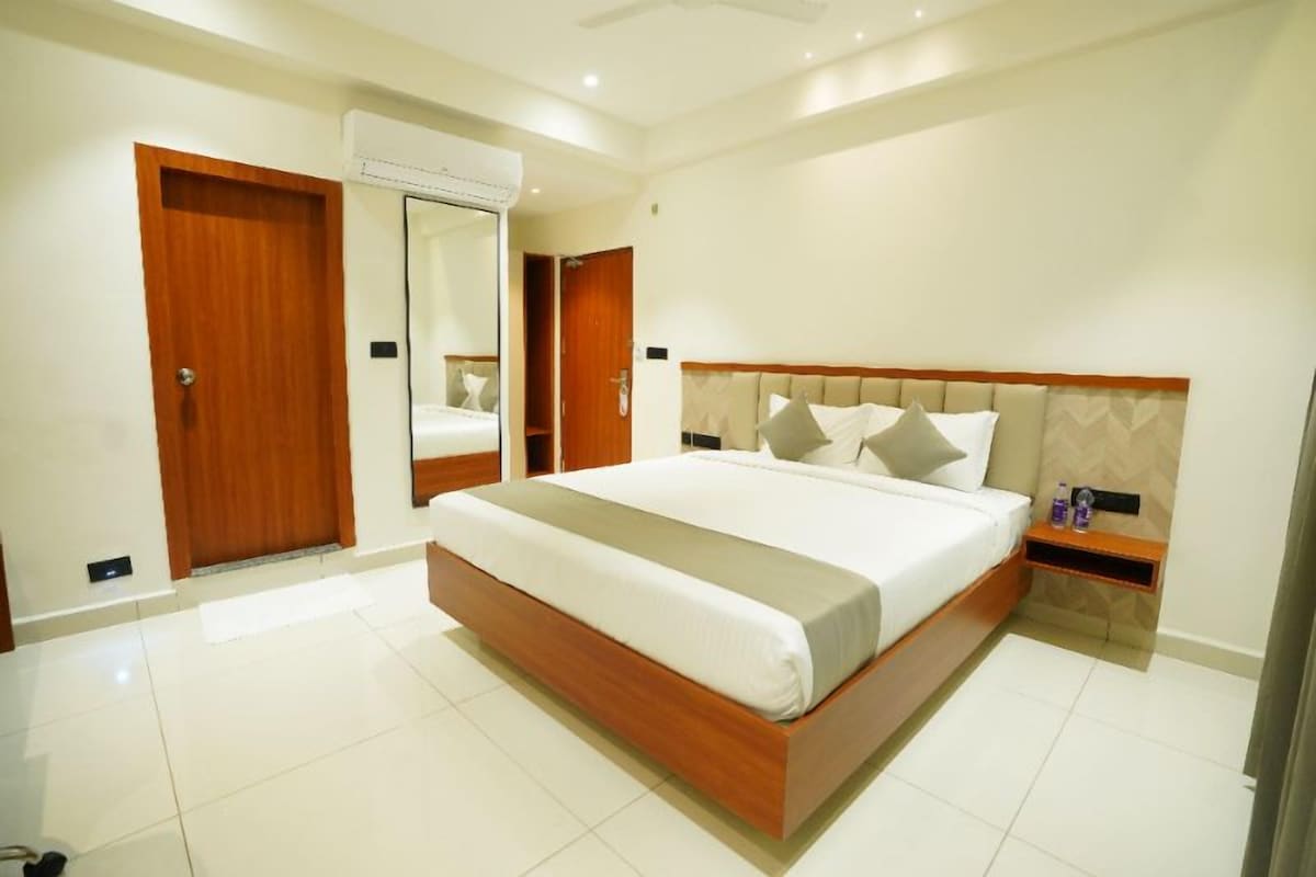 Quarto de hotel com uma cama grande, cabeceira de madeira, mesa de cabeceira e guarda-roupa.