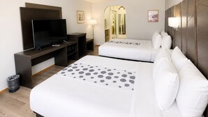 Ein Hotelzimmer mit zwei Betten, einem Fernseher, einem Schreibtisch und einem Spiegel.