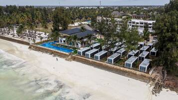 Un hotel frente a la playa con piscina, cabañas a la orilla del mar y una hilera de cabañas.