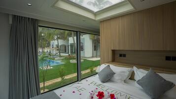 Une chambre avec une grande fenêtre, un lit avec des oreillers et une vue sur une piscine et la verdure environnante.