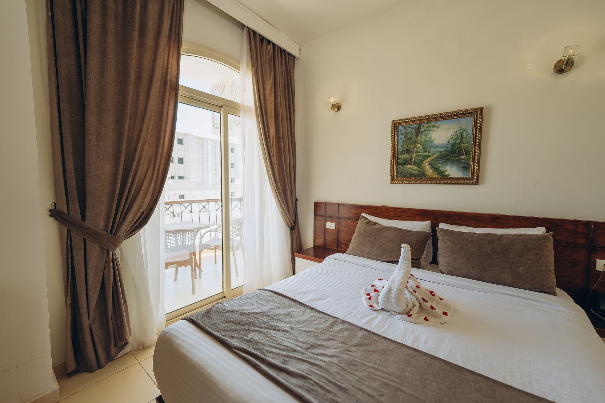 Een hotelkamer met een bed, gordijnen, een schilderij en uitzicht op het omliggende landschap.