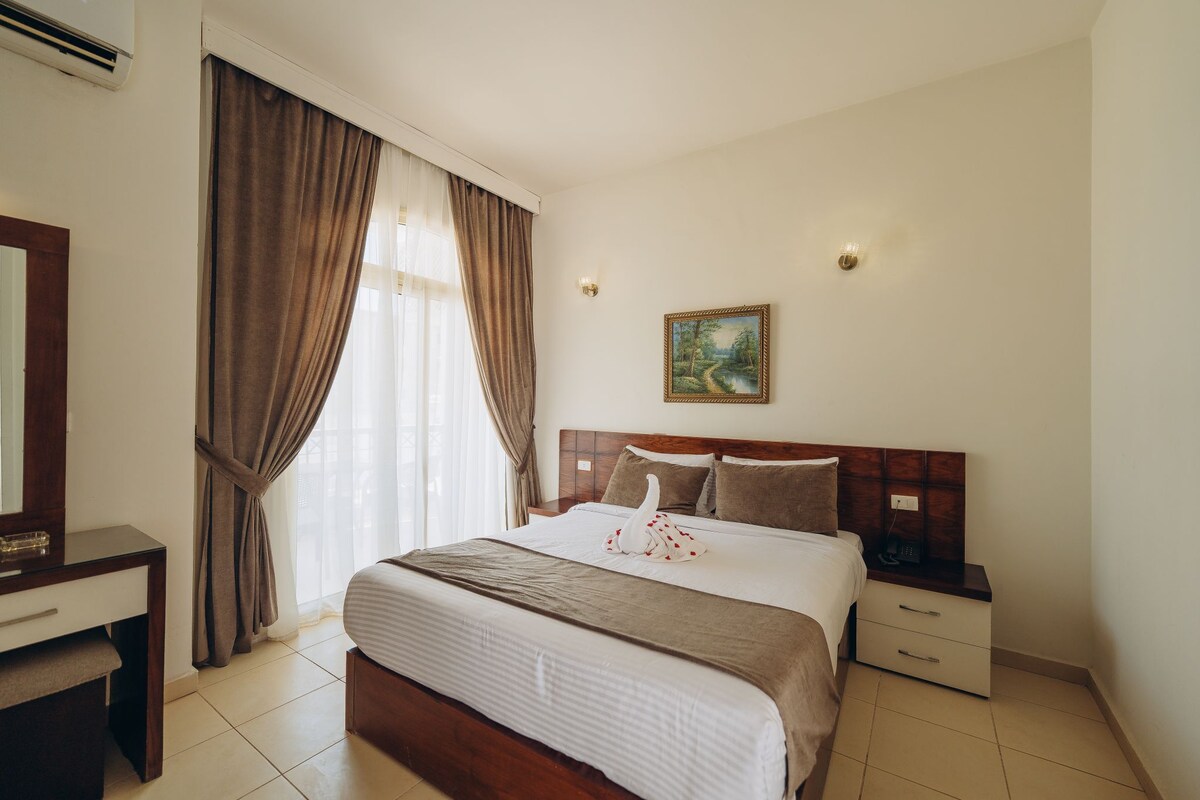 Una habitación de hotel con cama, mesita de noche, lámpara y un cuadro en la pared.
