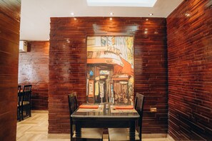Comedor con un mural de ladrillo, una mesa dispuesta para dos personas y sillas de madera.