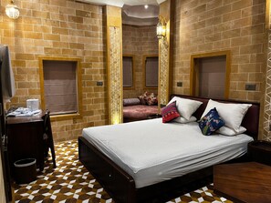 A hotel room with a check-in counter, a bed with patterned bedding, a decorative wall, and a patterned floor. - Gulaab Haveli (Jaisalmer)