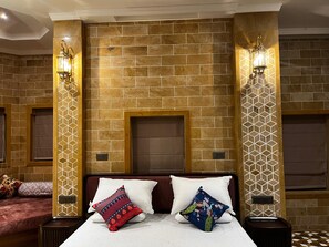 Habitación de hotel con pared de ladrillo, dos lámparas de noche, una cama con almohadas blancas y estampadas, y una mesita de noche con lámpara.