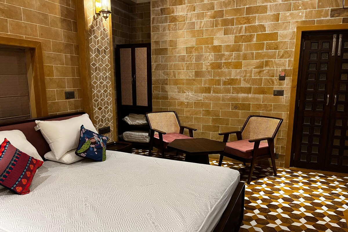 A hotel room with a bed, two chairs, a small table, and a door.