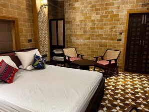 A hotel room with a bed, two chairs, a small table, and a door. - Gulaab Haveli (Jaisalmer)
