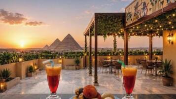 A rooftop bar with drinks and fruit, overlooking pyramids.
