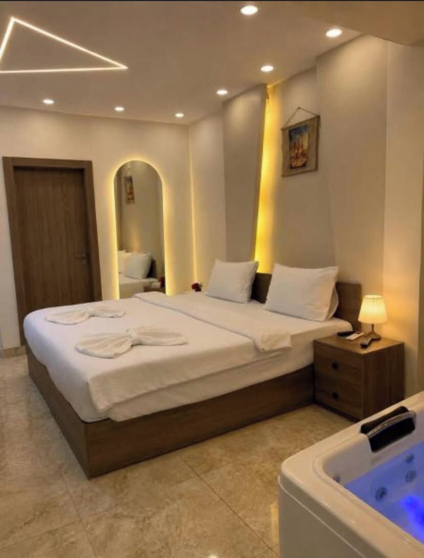 A modern hotel room with a large bed, bedside tables, a visible bathroom area, and a ceiling light fixture.
