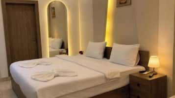 A modern hotel room with a large bed, bedside tables, a visible bathroom area, and a ceiling light fixture.