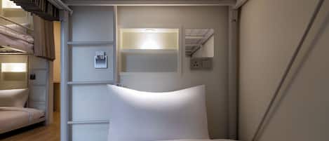 A hotel room with a bunk bed, a bedside table, a wall-mounted light, and a mirror.